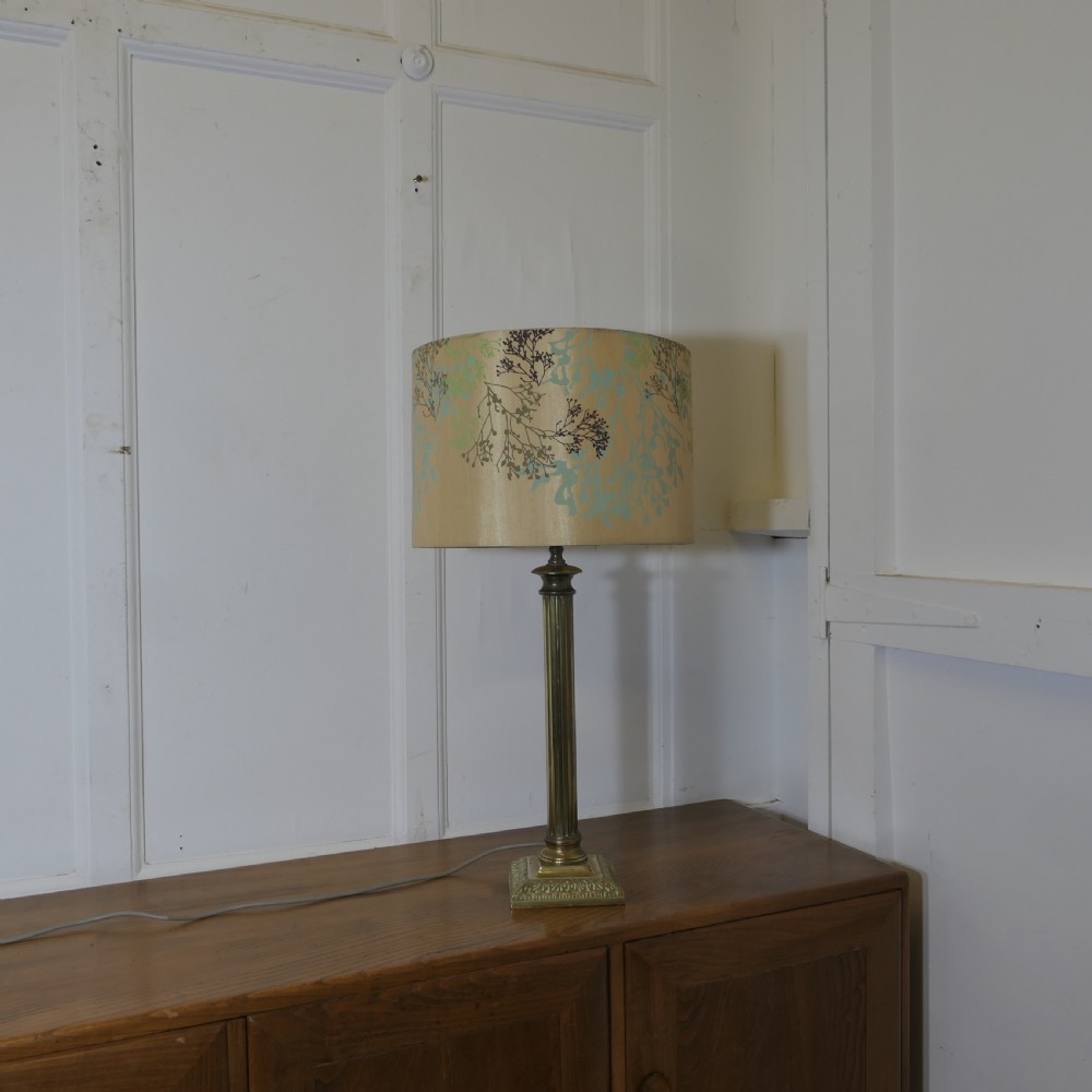 A tall brass table lamp featuring a fluted column stem on a stepped square base, topped with a cylindrical cream shade patterned with botanical motifs. View VII