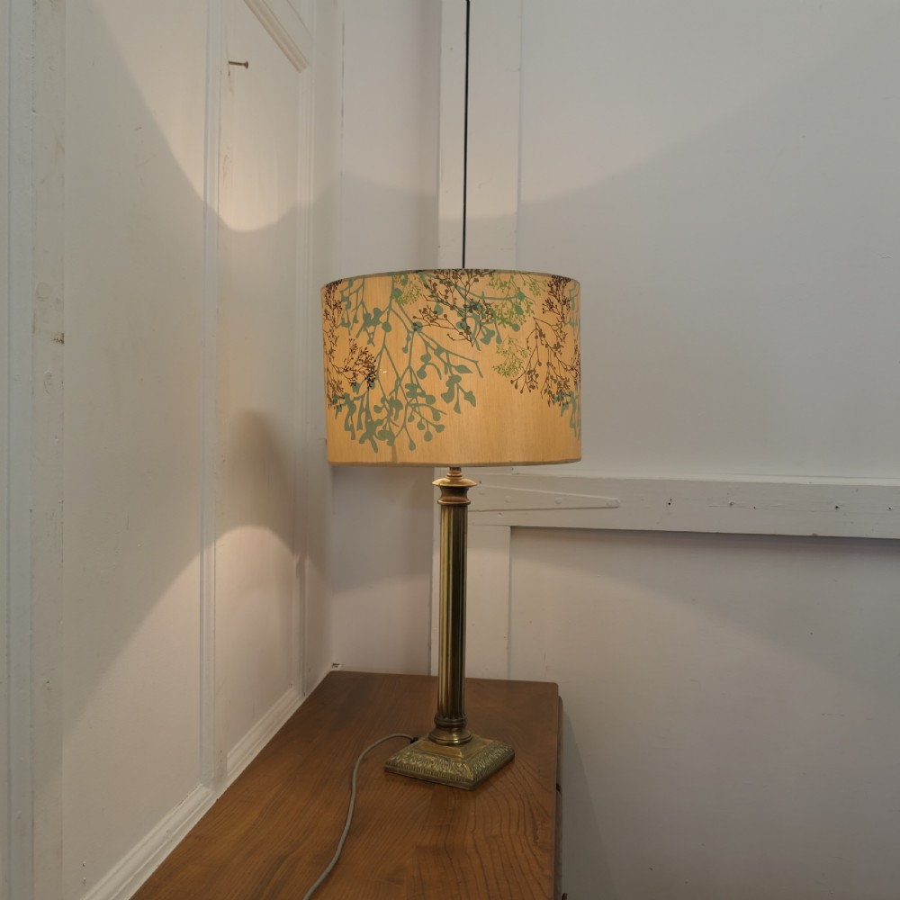 A tall brass table lamp featuring a fluted column stem on a stepped square base, topped with a cylindrical cream shade patterned with botanical motifs. View VIII