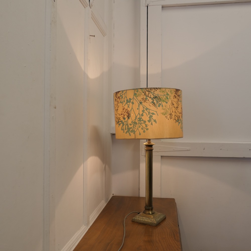 A tall brass table lamp featuring a fluted column stem on a stepped square base, topped with a cylindrical cream shade patterned with botanical motifs. View IX