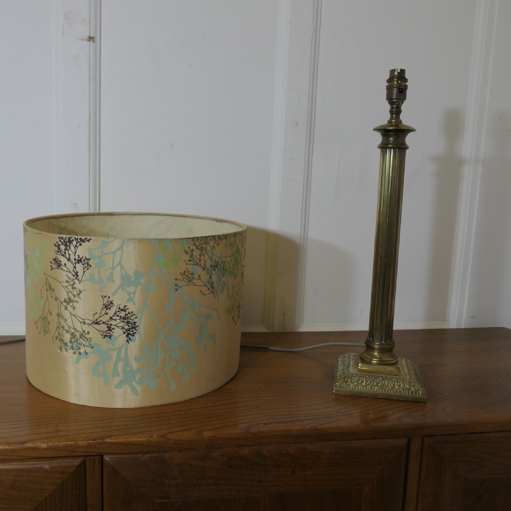 A tall brass table lamp featuring a fluted column stem on a stepped square base, topped with a cylindrical cream shade patterned with botanical motifs. View X