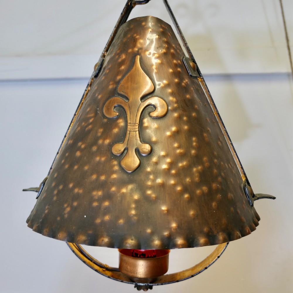 A hand-hammered copper conical pendant lantern featuring an applied fleur-de-lis motif suspended from a wrought iron frame. View III