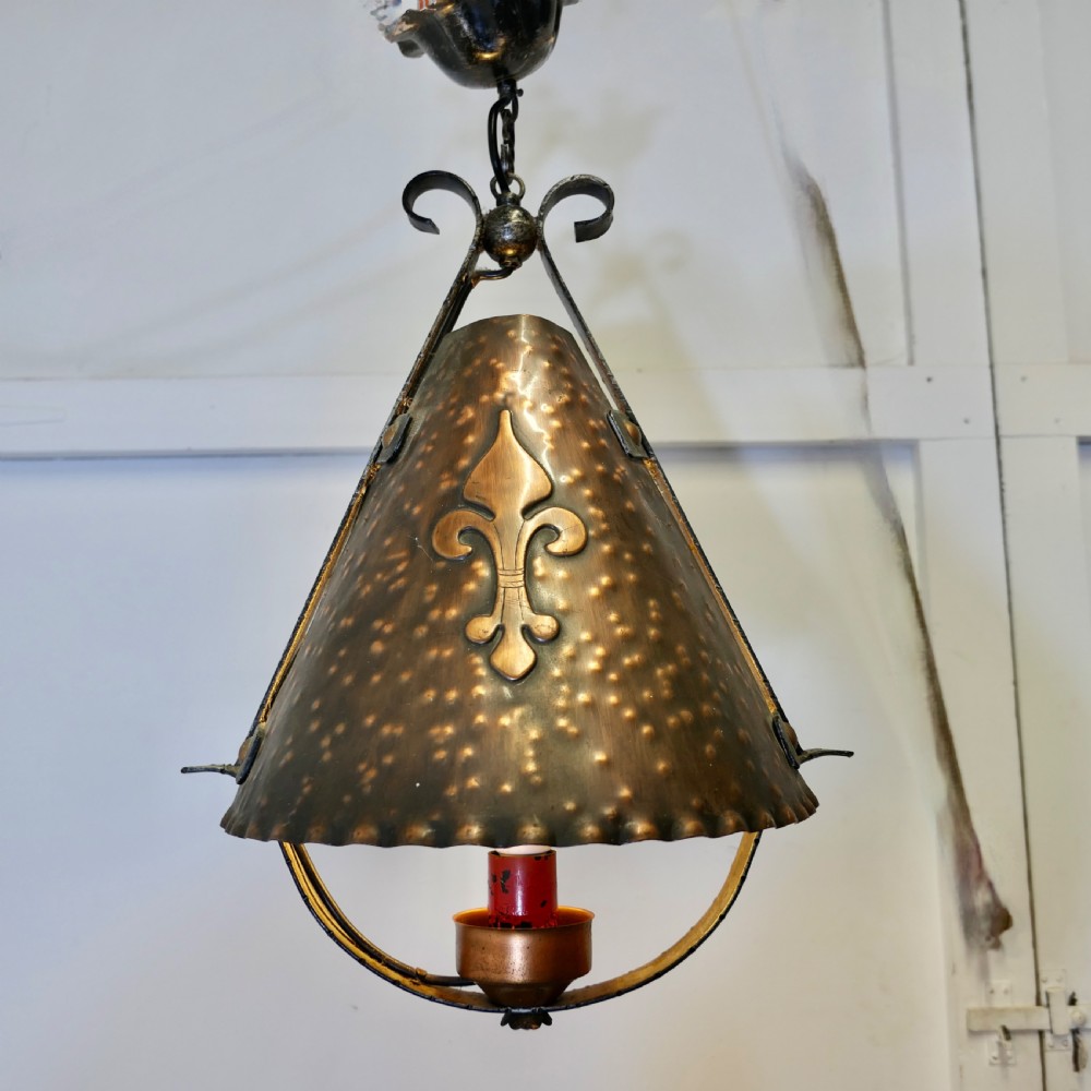 A hand-hammered copper conical pendant lantern featuring an applied fleur-de-lis motif suspended from a wrought iron frame. View IV