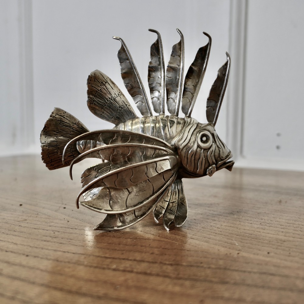 A sterling silver lionfish model featuring dramatic fan-like dorsal spines and engraved scales displayed on a wooden surface.