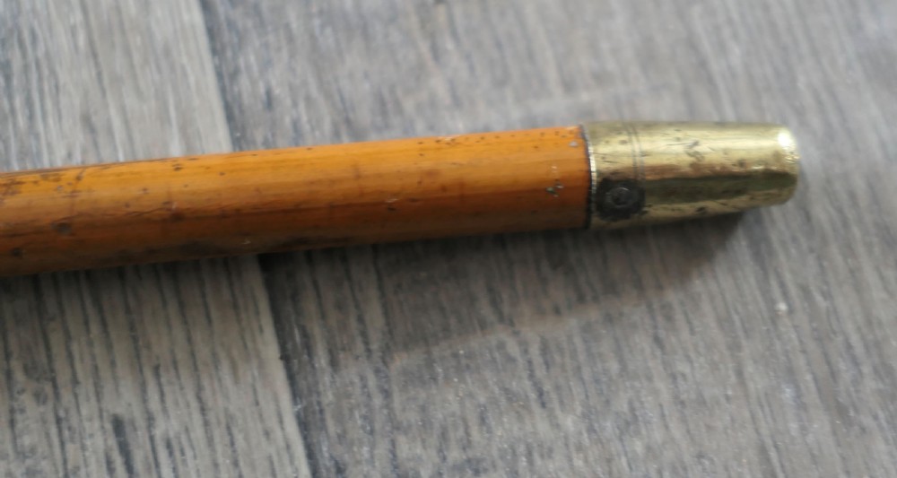 A slender light brown cane swagger stick featuring a silver-toned embossed metal cap at the top and a metal tip ferrule. View II