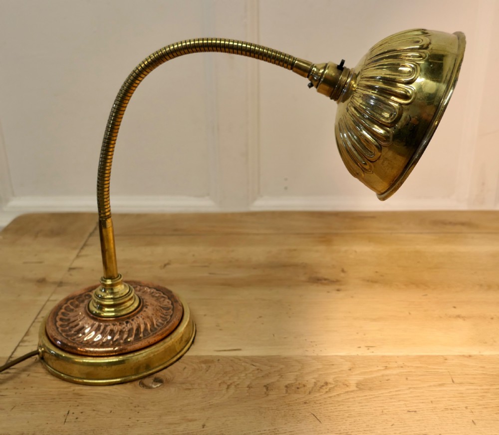 An Art Deco desk lamp featuring a flexible gooseneck arm, a ribbed brass shade, and a circular copper and brass base.