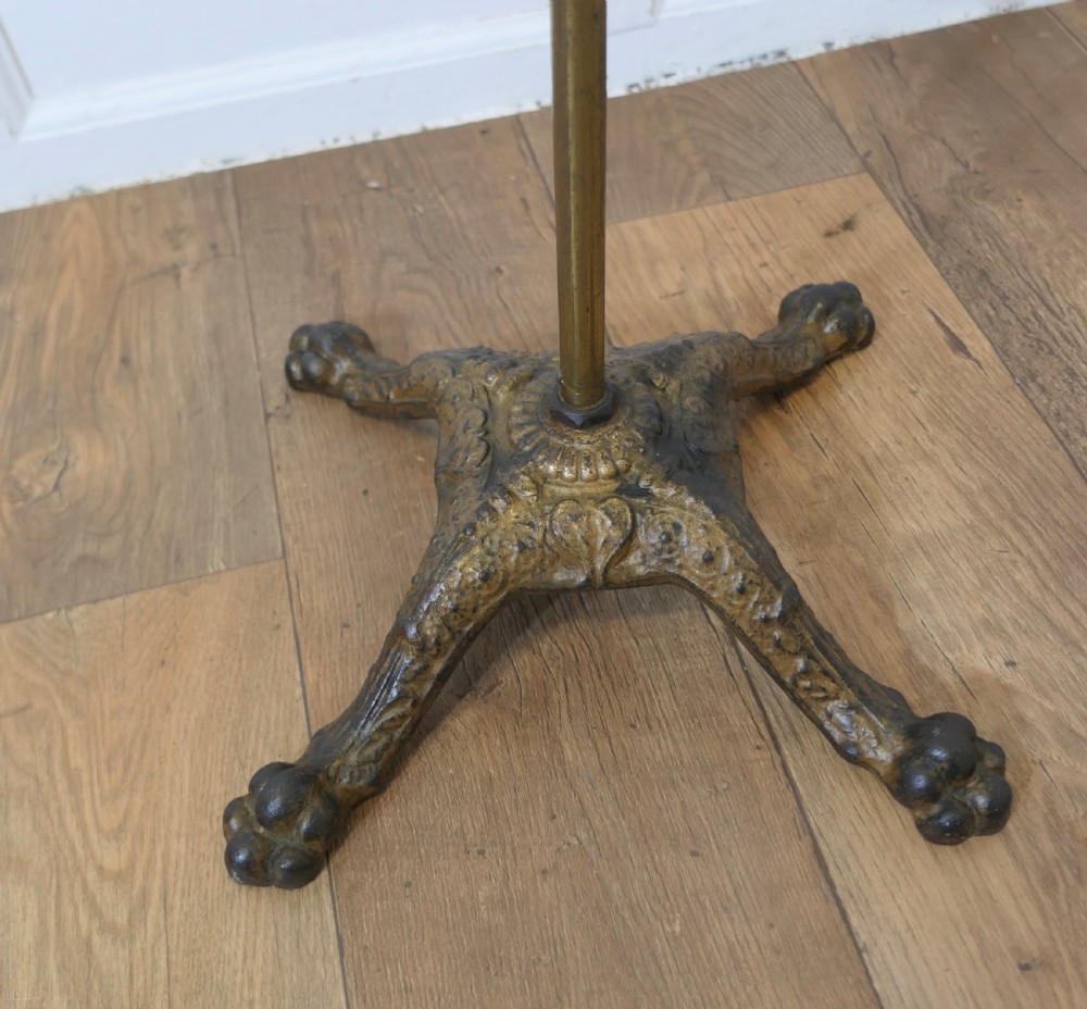 A floor-standing adjustable brass reading stand featuring a dark wooden tilted book rest, an articulated extension arm, and a four-legged cast iron claw foot base. View VI