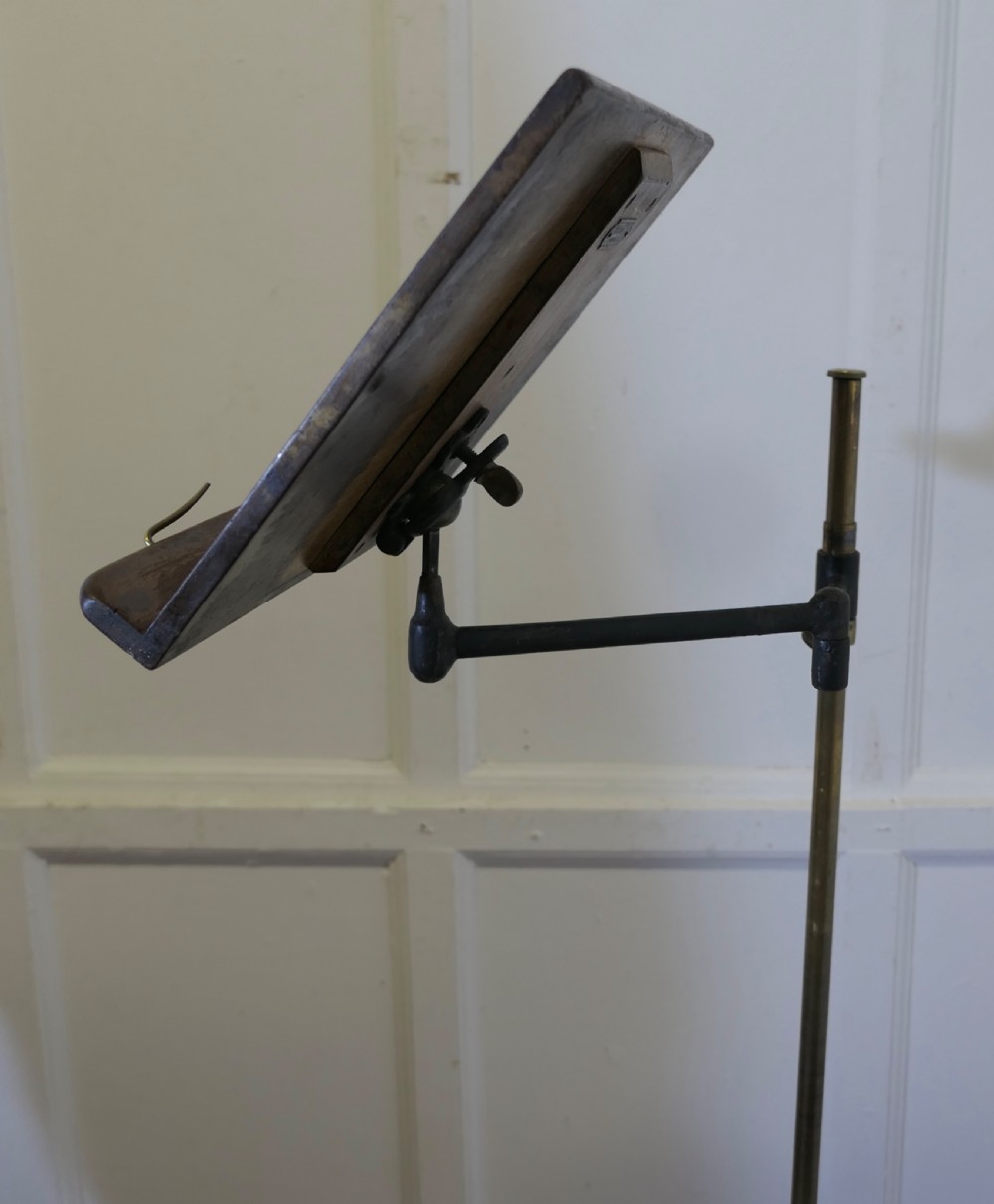 A floor-standing adjustable brass reading stand featuring a dark wooden tilted book rest, an articulated extension arm, and a four-legged cast iron claw foot base. View VII