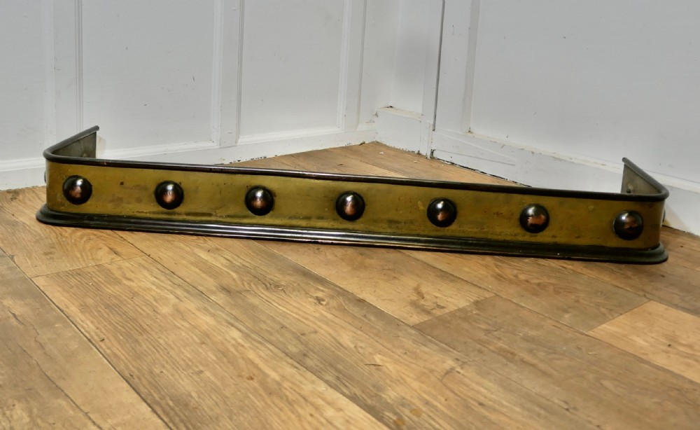 An antique Arts and Crafts brass fireplace fender featuring a row of raised copper domed bosses along the front panel with dark metal border trims.
