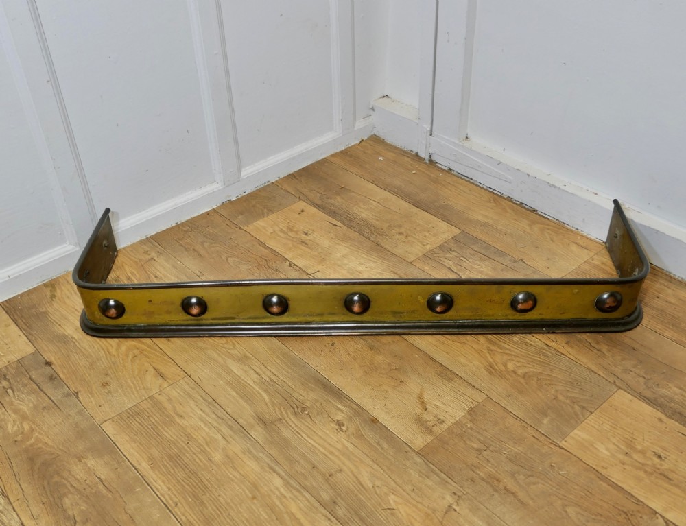 An antique Arts and Crafts brass fireplace fender featuring a row of raised copper domed bosses along the front panel with dark metal border trims. View II