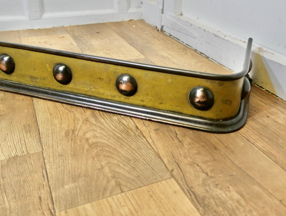 An antique Arts and Crafts brass fireplace fender featuring a row of raised copper domed bosses along the front panel with dark metal border trims. View III