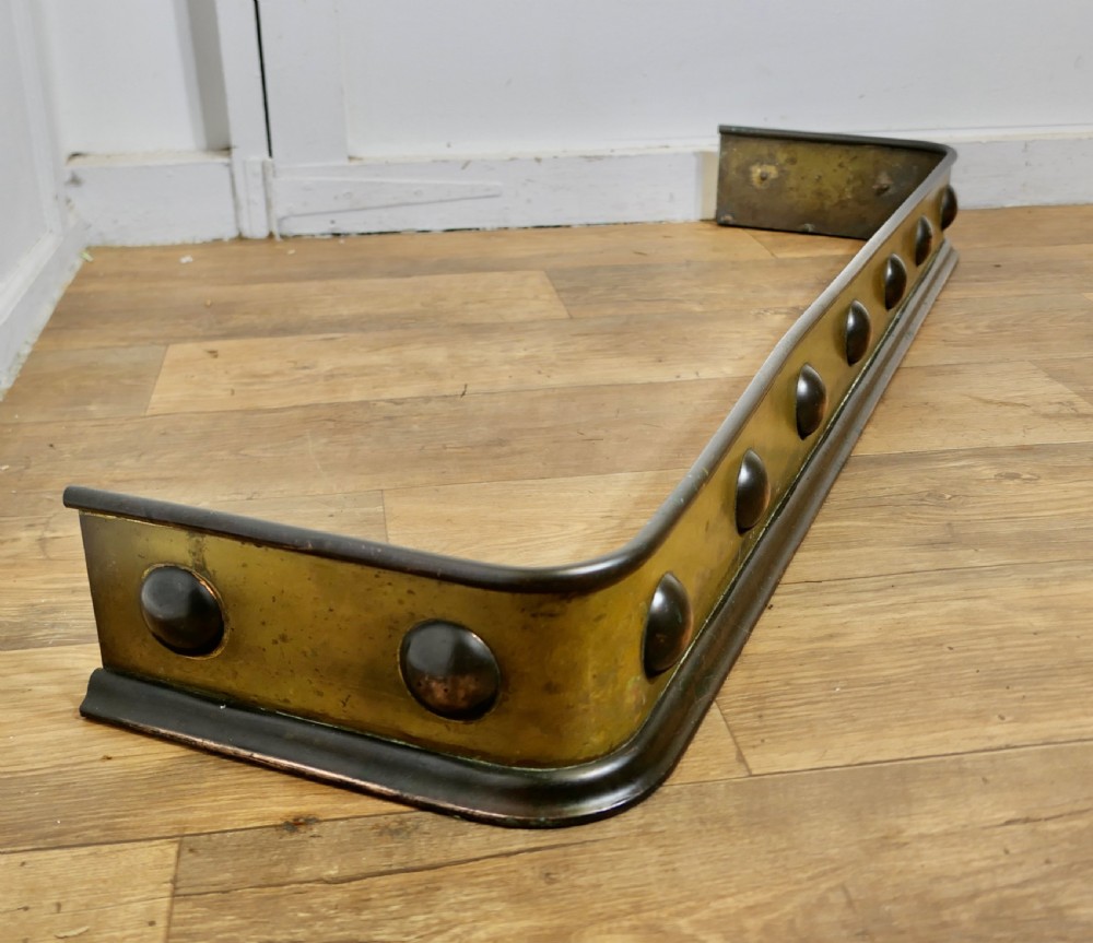 An antique Arts and Crafts brass fireplace fender featuring a row of raised copper domed bosses along the front panel with dark metal border trims. View IV