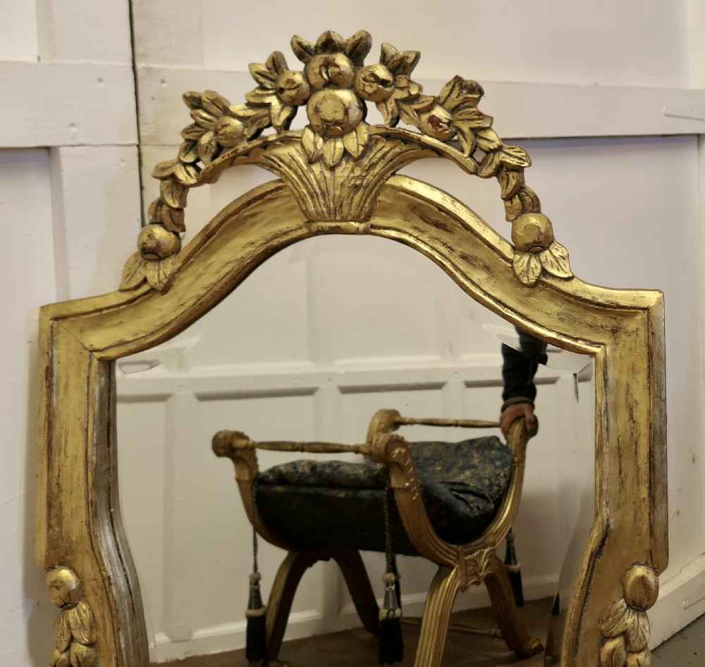 An ornate French giltwood wall mirror featuring a carved floral cresting, contoured sides with leaf motifs, and a gilded finish. View V