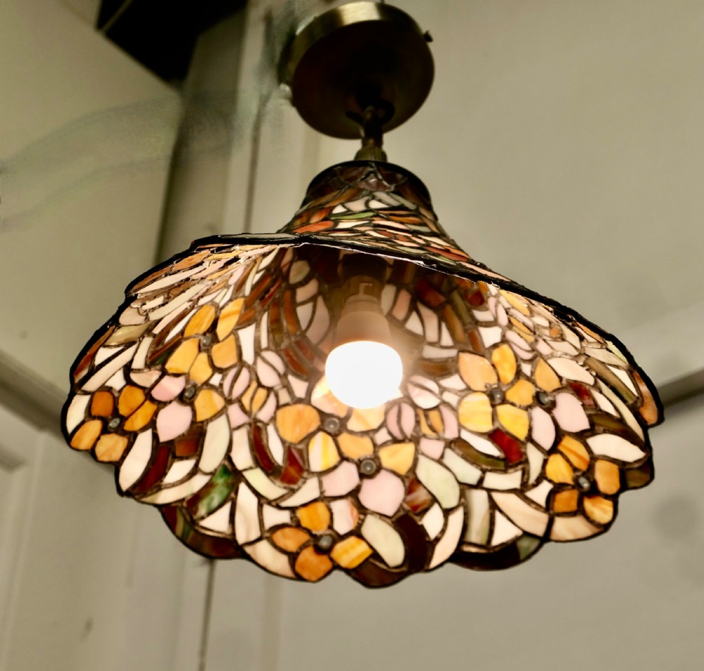 A conical Arts and Crafts stained glass lampshade featuring an amber and cream floral pattern with a scalloped lower edge and brass ceiling fittings. View II