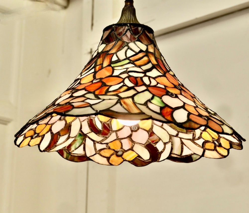 A conical Arts and Crafts stained glass lampshade featuring an amber and cream floral pattern with a scalloped lower edge and brass ceiling fittings. View III