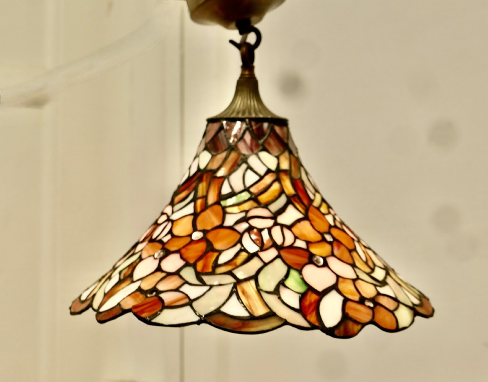 A conical Arts and Crafts stained glass lampshade featuring an amber and cream floral pattern with a scalloped lower edge and brass ceiling fittings. View V