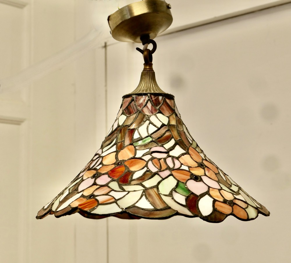 A conical Arts and Crafts stained glass lampshade featuring an amber and cream floral pattern with a scalloped lower edge and brass ceiling fittings. View VII