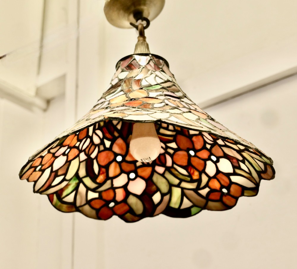 A conical Arts and Crafts stained glass lampshade featuring an amber and cream floral pattern with a scalloped lower edge and brass ceiling fittings. View VIII