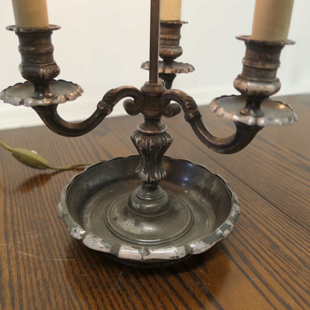 A silver-plated French bouillotte desk lamp featuring a green tole shade with gold scroll detailing and three candlestick lights set in a dished base. View V