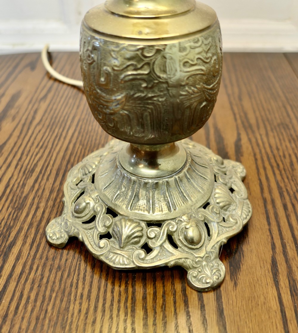 A tall embossed brass table lamp featuring a cast footed base and an embroidered cream tapered shade. View III