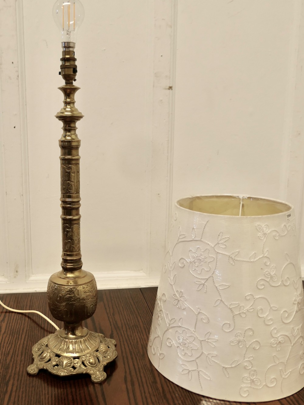 A tall embossed brass table lamp featuring a cast footed base and an embroidered cream tapered shade. View X