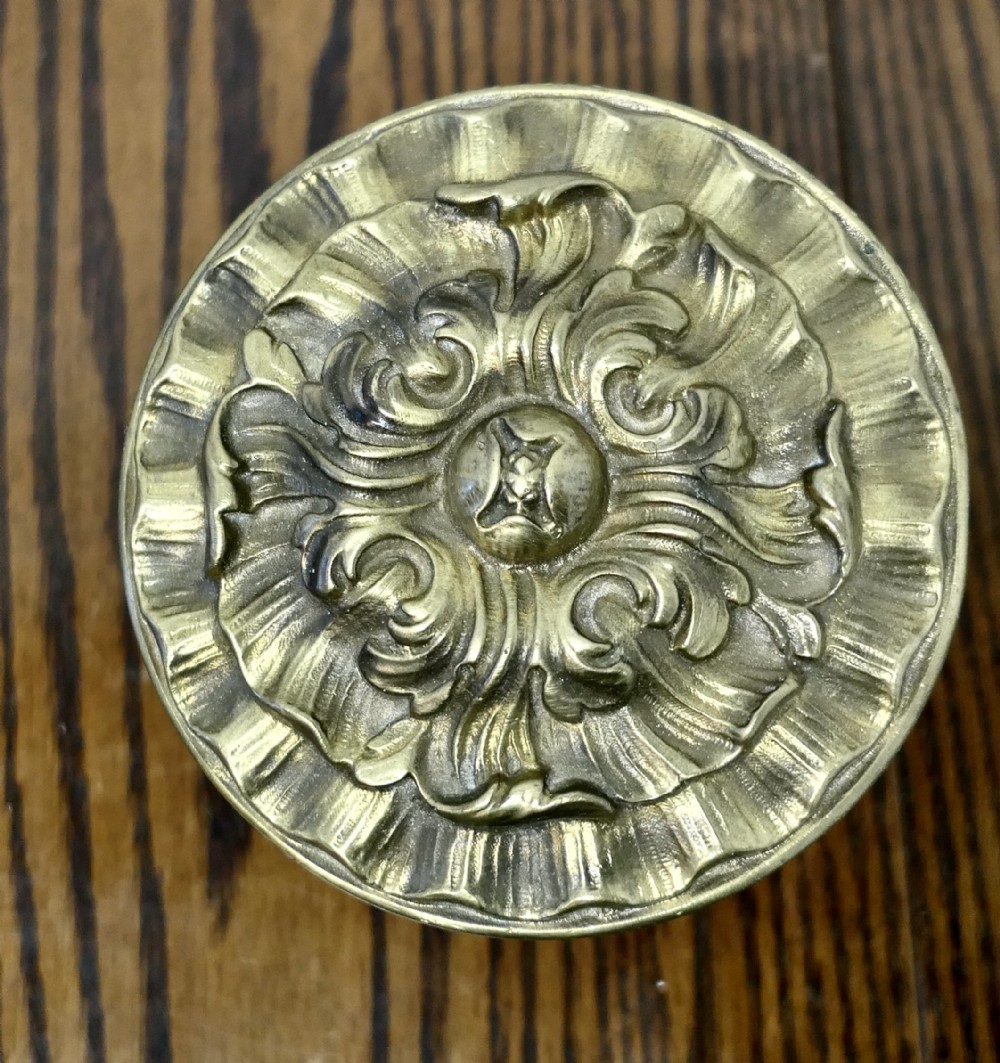 A circular embossed brass door knob featuring an intricate floral and scrollwork design.