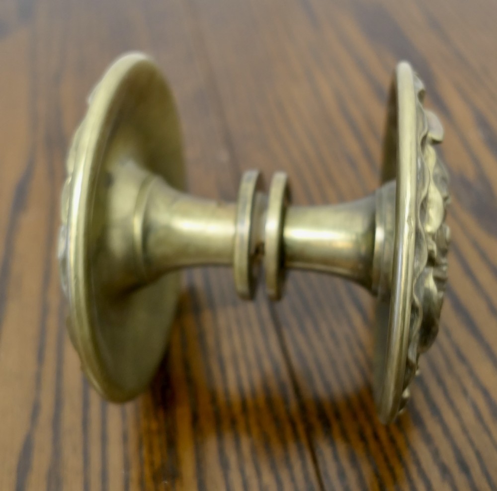 A circular embossed brass door knob featuring an intricate floral and scrollwork design. View III