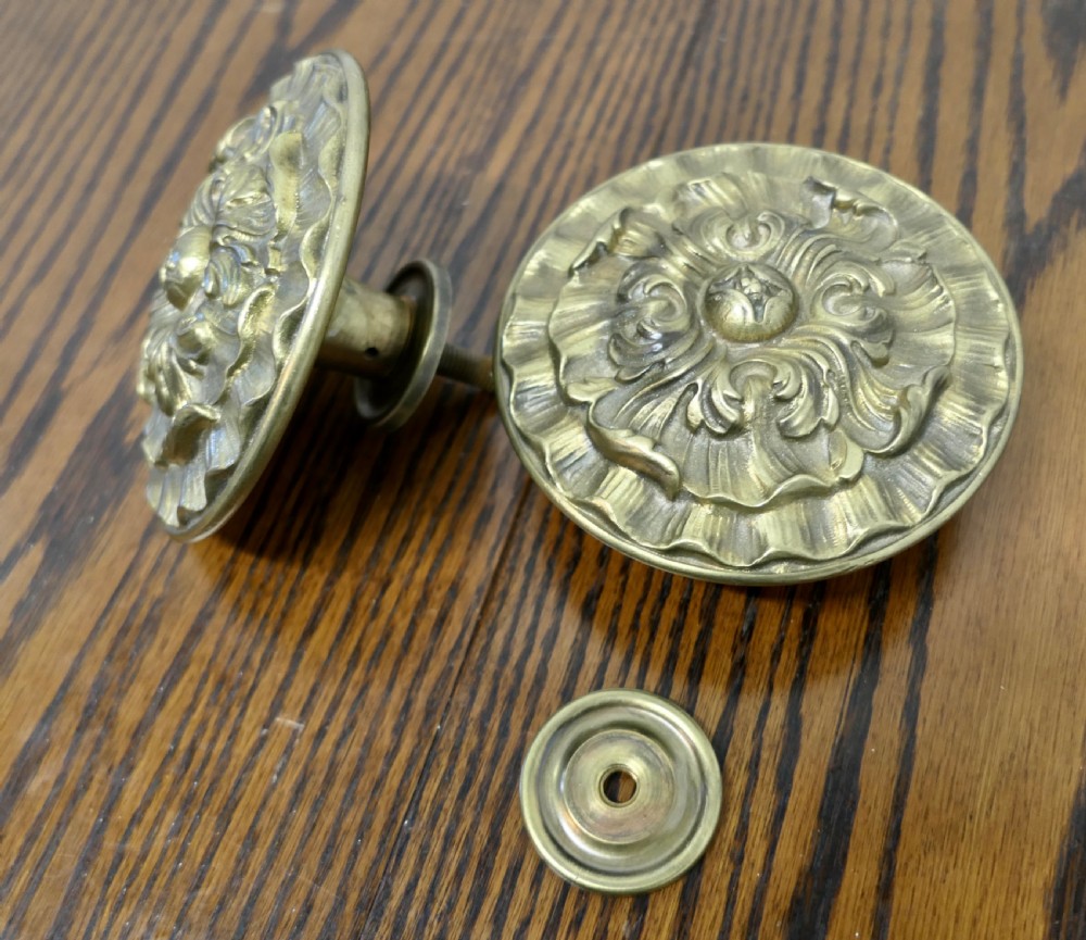 A circular embossed brass door knob featuring an intricate floral and scrollwork design. View IV