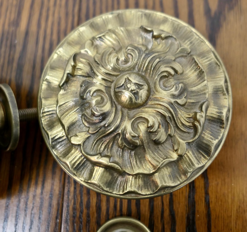 A circular embossed brass door knob featuring an intricate floral and scrollwork design. View V