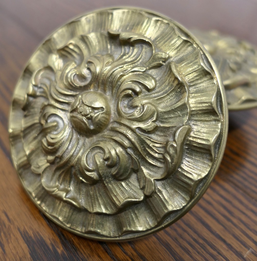 A circular embossed brass door knob featuring an intricate floral and scrollwork design. View VI