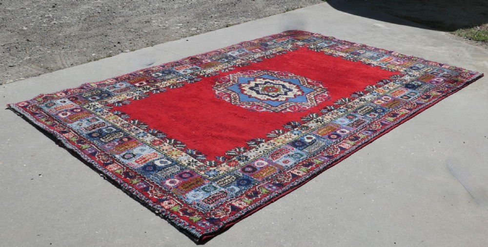 A red hand-knotted wool rug featuring a large central blue and cream star medallion surrounded by an intricate multi-coloured geometric border.