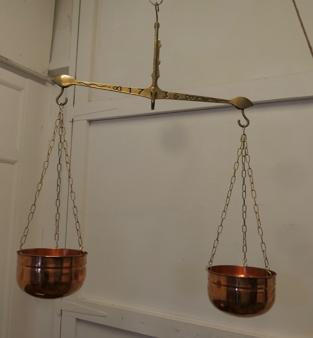 A pair of polished copper pans suspended by brass chains from an engraved brass balance beam.