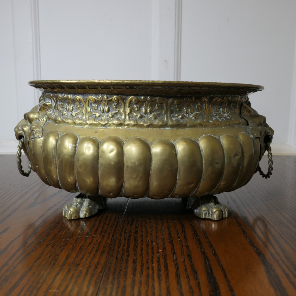 An oval antique brass jardiniere featuring gadrooned lower detail, lion mask handles with drop rings, paw feet, and a removable internal metal liner. View II