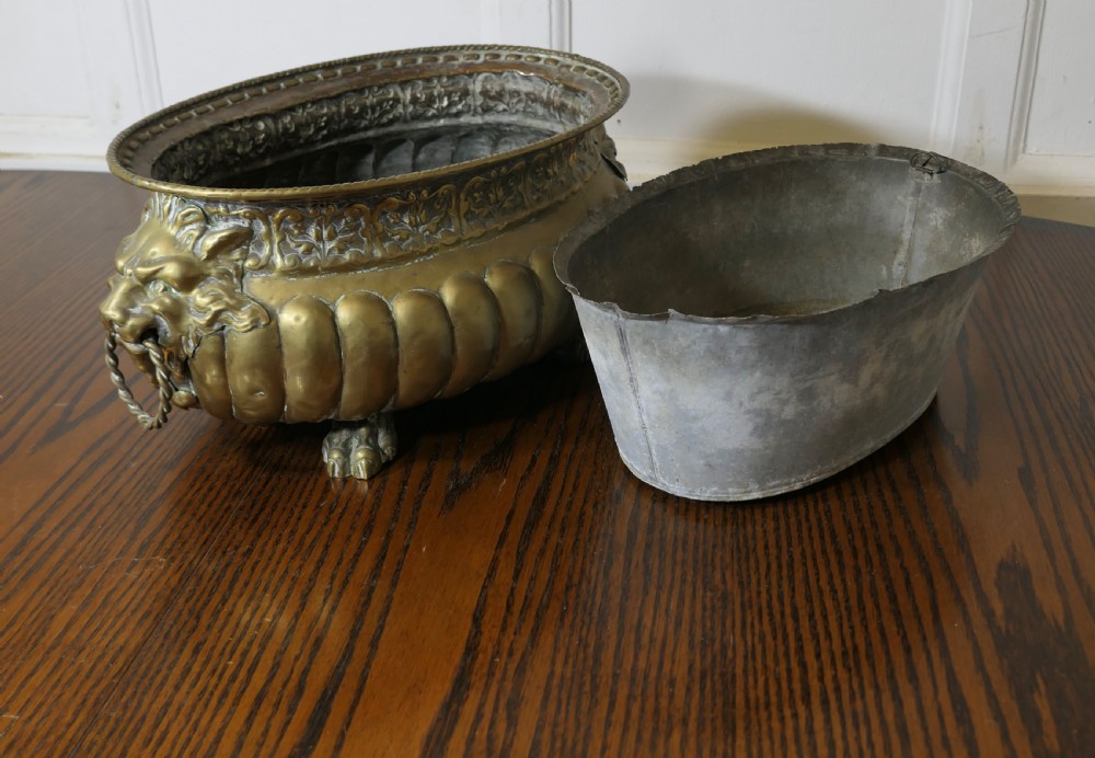An oval antique brass jardiniere featuring gadrooned lower detail, lion mask handles with drop rings, paw feet, and a removable internal metal liner. View VI