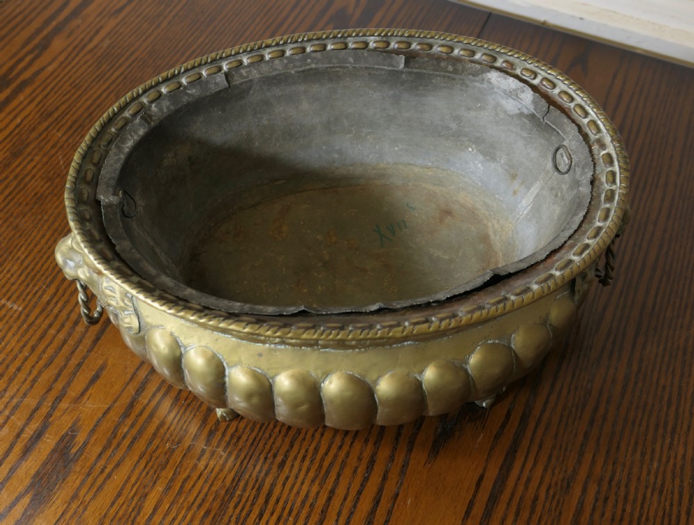An oval antique brass jardiniere featuring gadrooned lower detail, lion mask handles with drop rings, paw feet, and a removable internal metal liner. View VII
