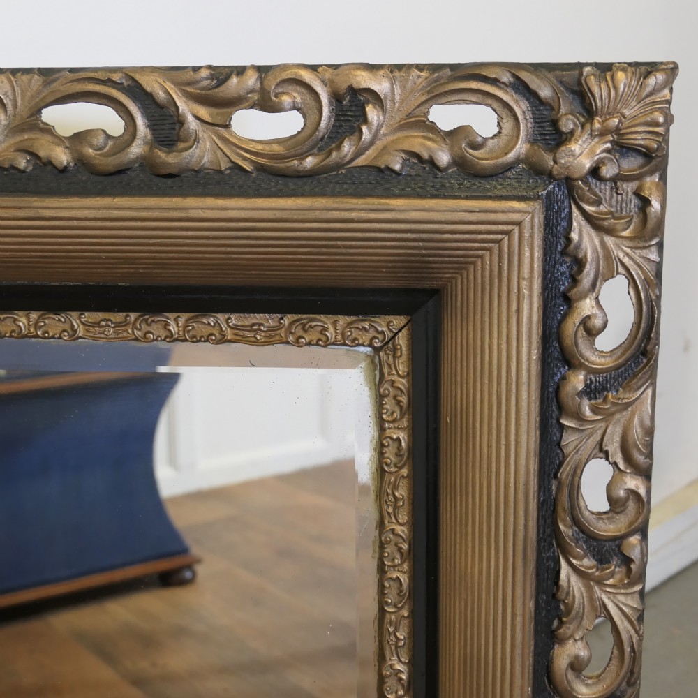 A large rectangular wall mirror featuring an ornate dark gilt frame with openwork scroll carving, a reeded inner moulding, and dark accents. View IV