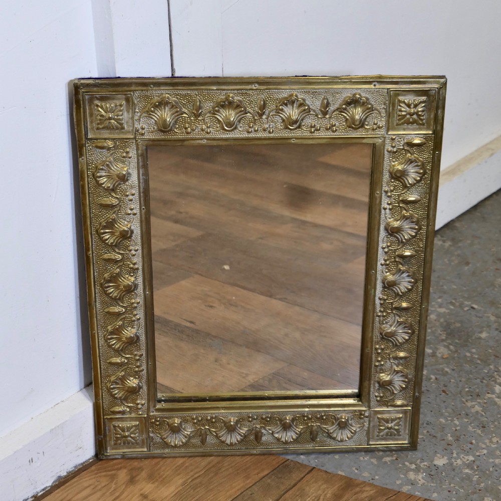 A rectangular wall mirror featuring an embossed brass frame decorated with shell motifs and stippled texture.