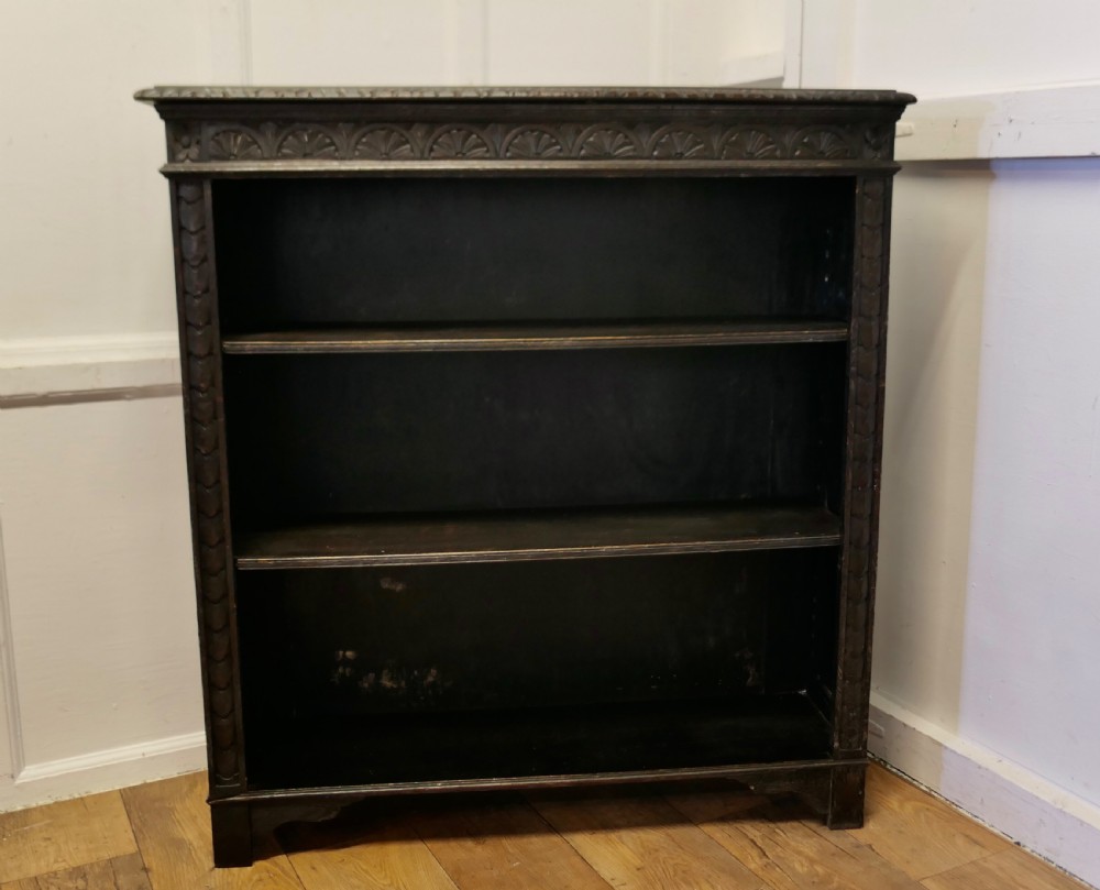 A dark carved oak open bookcase featuring a decorative carved frieze and three open shelves.