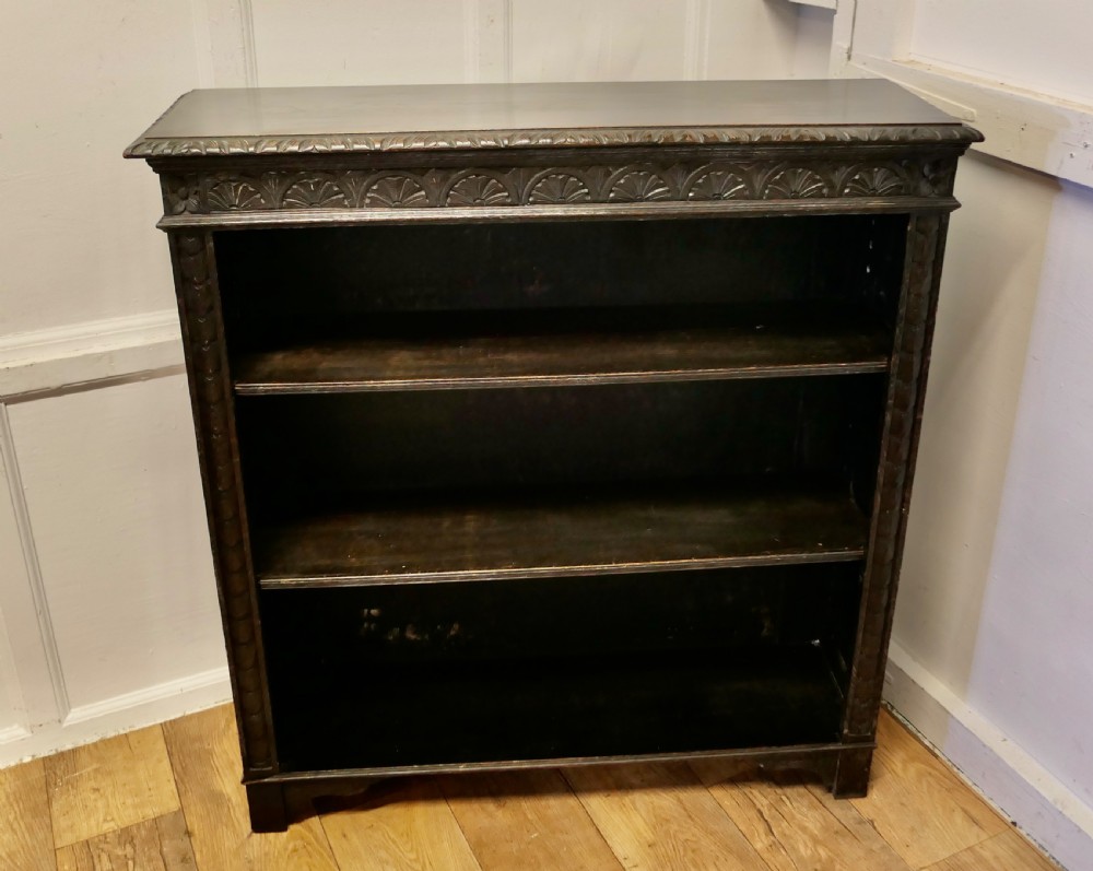 A dark carved oak open bookcase featuring a decorative carved frieze and three open shelves. View II