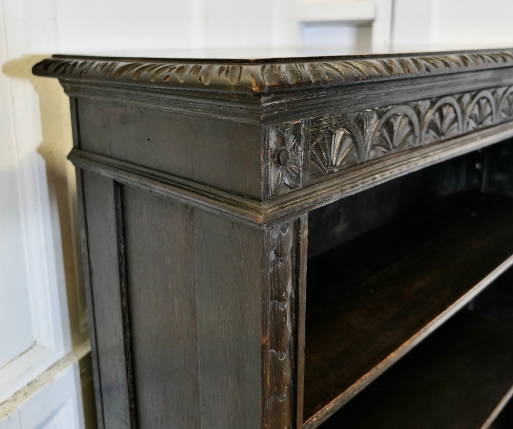 A dark carved oak open bookcase featuring a decorative carved frieze and three open shelves. View IV