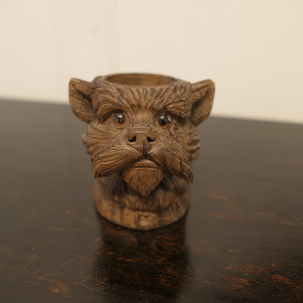 A hand-carved wooden head of a Scottish terrier with glass eyes and carved fur details.