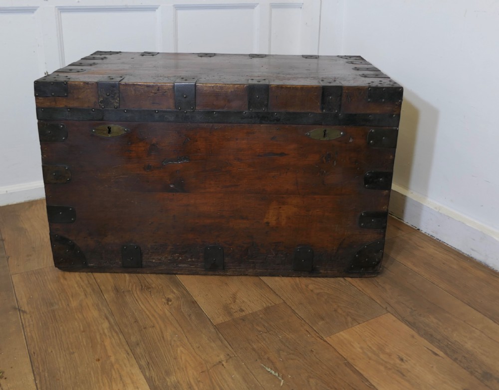 A large dark wood travel trunk with heavy black iron straps, corner metalwork, and two brass keyhole plates.