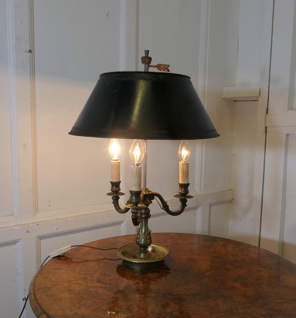 A French triple-light bouillotte lamp featuring a dark green painted toleware shade, three brass candle arms, and a dished brass tray base.