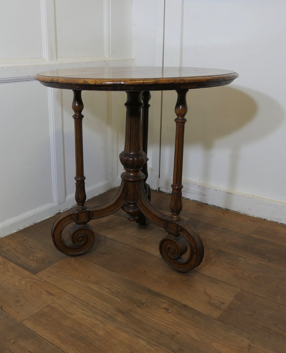 A nineteenth-century burr walnut wine table featuring a circular top supported by turned pillars and carved scroll feet.