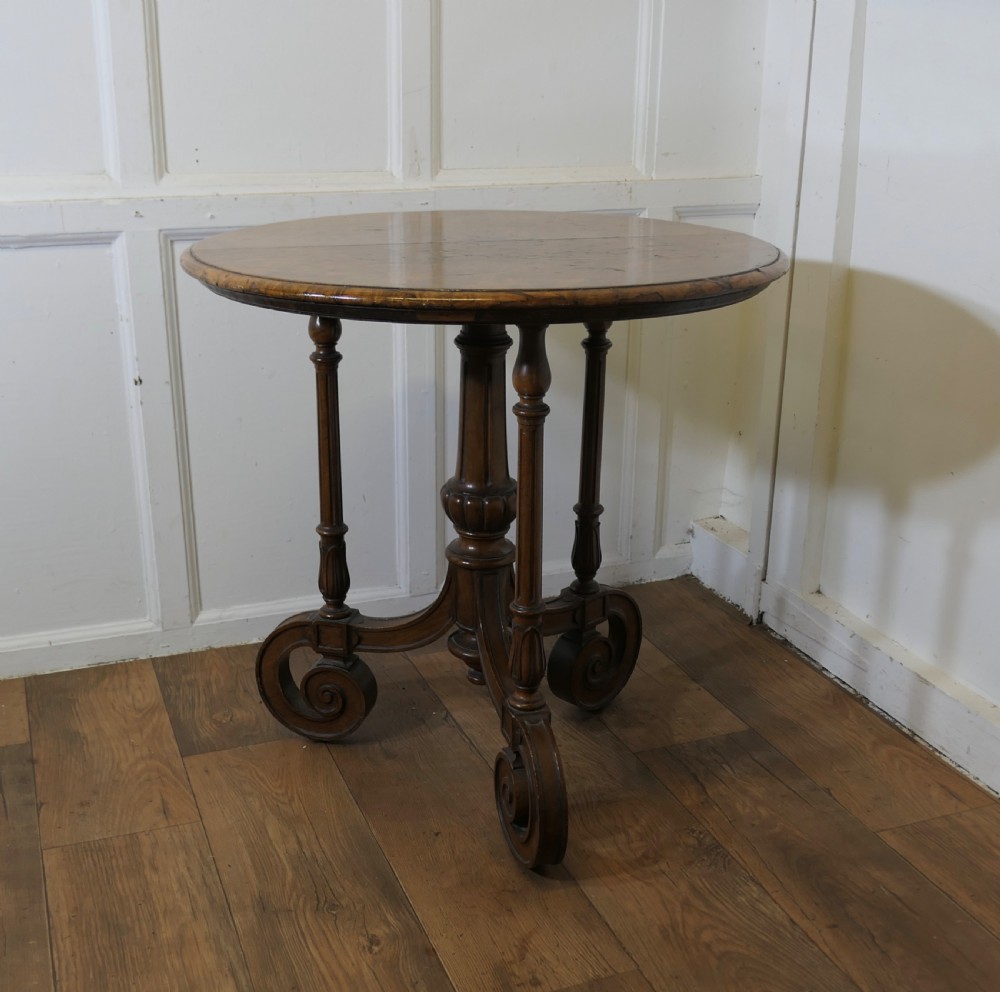 A nineteenth-century burr walnut wine table featuring a circular top supported by turned pillars and carved scroll feet. View II