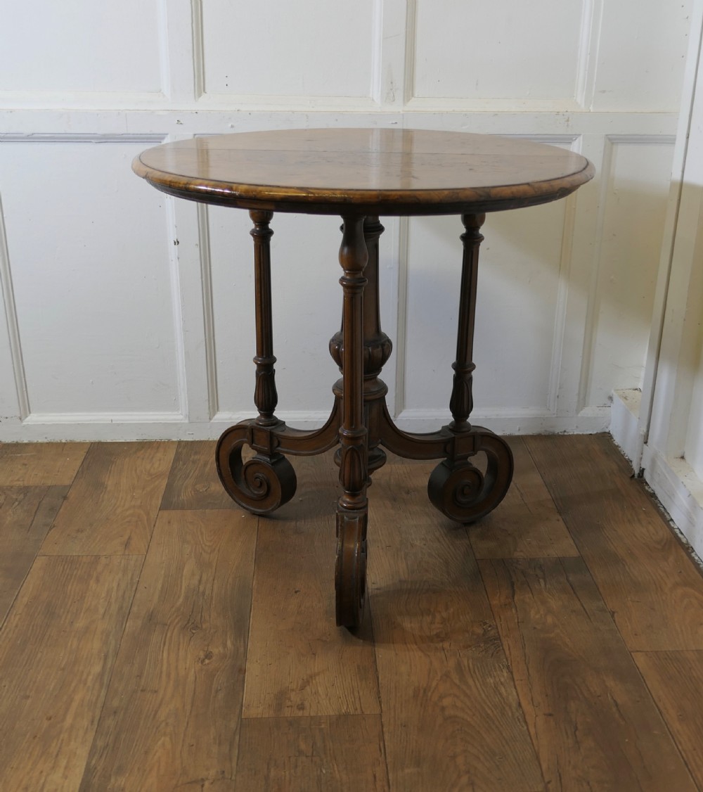 A nineteenth-century burr walnut wine table featuring a circular top supported by turned pillars and carved scroll feet. View V