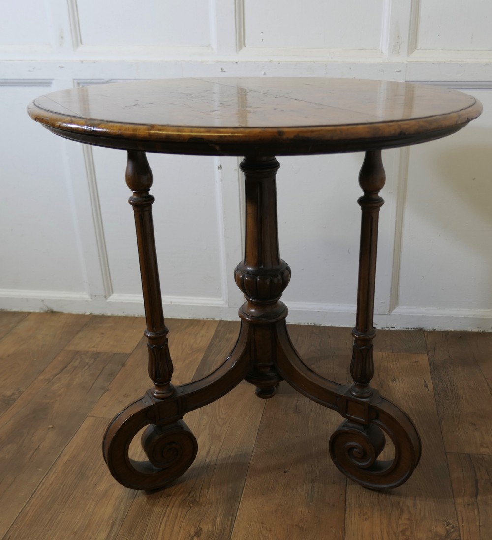 A nineteenth-century burr walnut wine table featuring a circular top supported by turned pillars and carved scroll feet. View VII