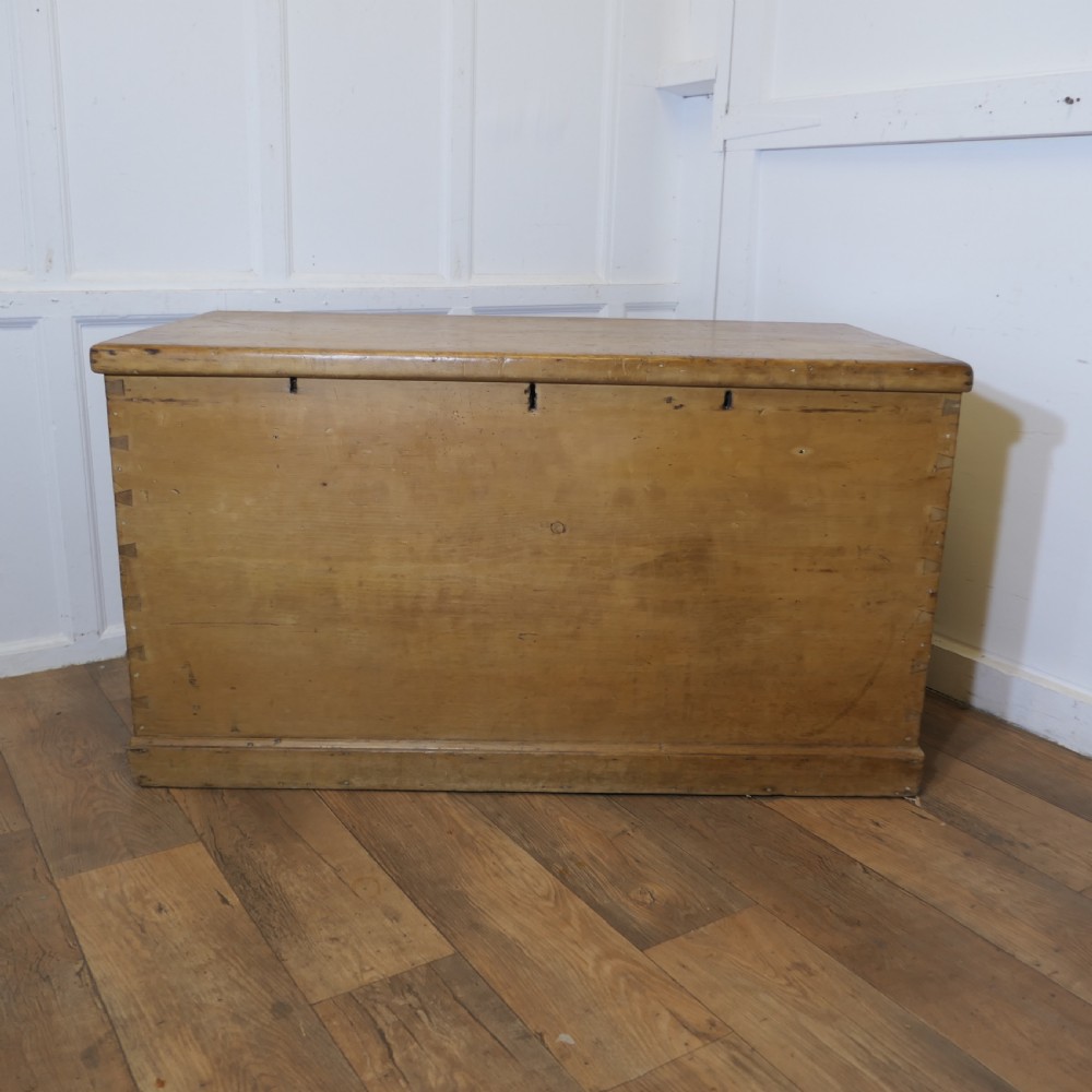 A large rectangular Victorian polished pine blanket box with visible dovetail joints, a flat hinged lid, and a thick wooden plinth base.