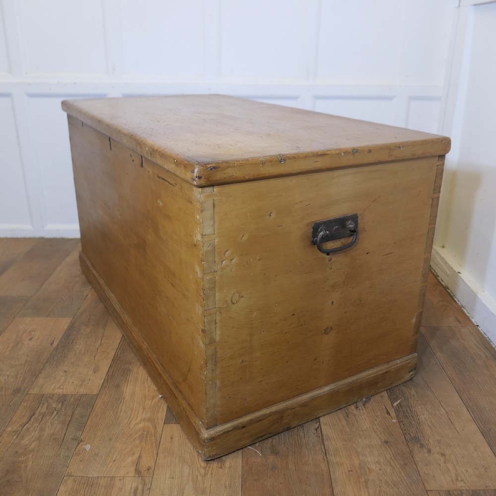 A large rectangular Victorian polished pine blanket box with visible dovetail joints, a flat hinged lid, and a thick wooden plinth base. View V