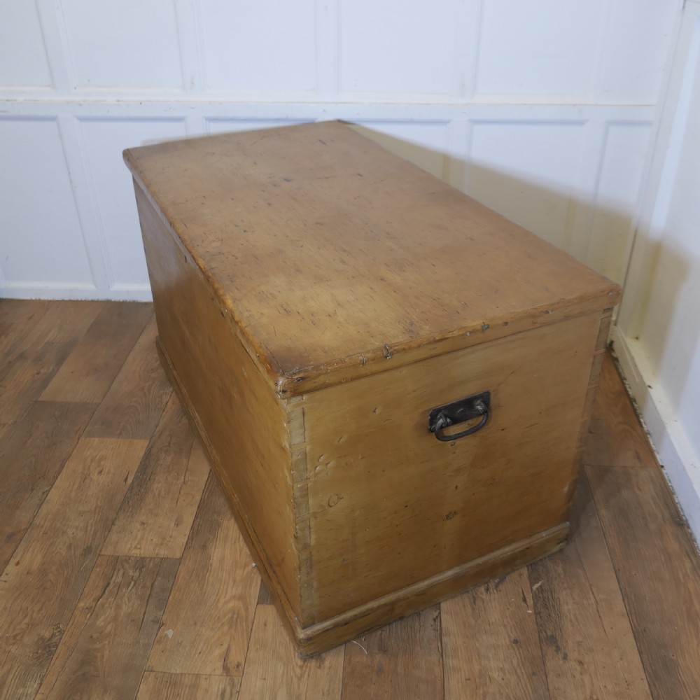 A large rectangular Victorian polished pine blanket box with visible dovetail joints, a flat hinged lid, and a thick wooden plinth base. View VI