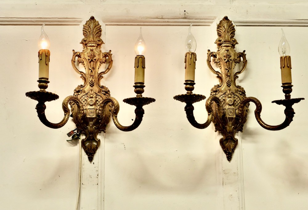 A pair of ornate cast brass twin-arm wall sconces featuring Rococo scrollwork and faux candle drip sleeves. View II